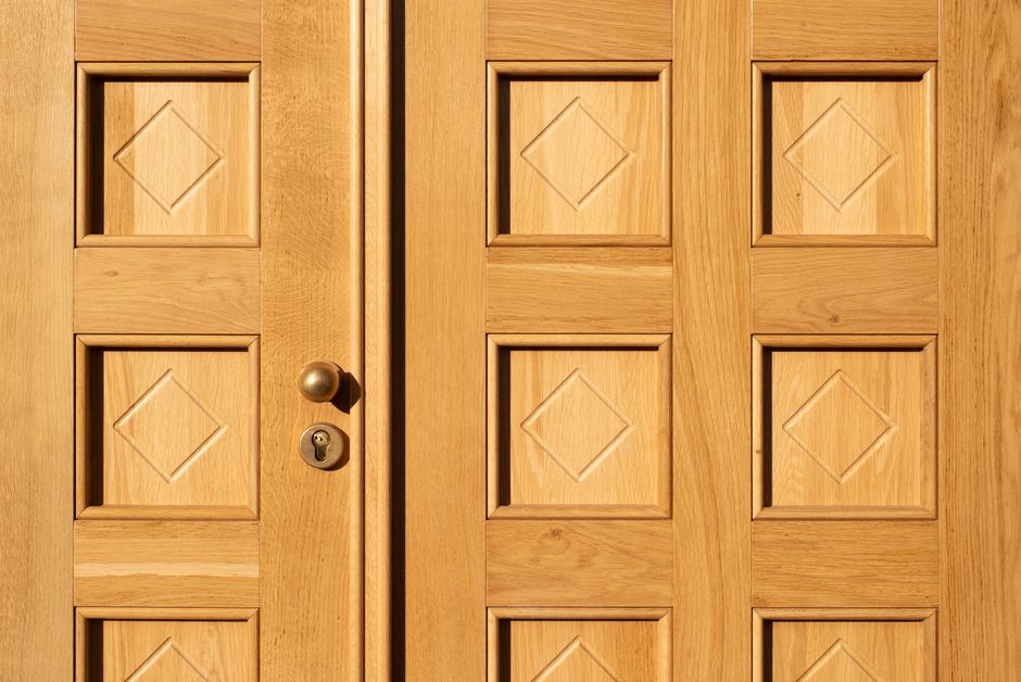 Vizinhança Solidária — Close-up of a wooden door featuring geometric diamond patterns and a brass handle.